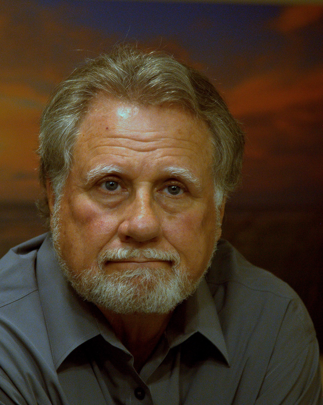 Grey haired white man with dress shirt in front of a red photo background